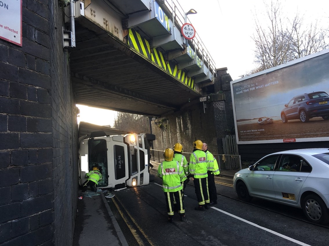 Fire crews standing under a bridge with a lorry on its side after striking a bridge