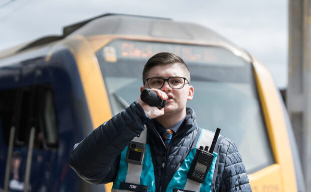 Station controller Tom in his station uniform, speaking into a tannoy.